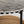 Close-up of a round table with a black and off-white geometric inlay pattern on the tabletop and a black metal leg, with a woven chair partially visible underneath.