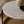 A round nesting side table with a gray and cream leaf patterned top, a black metal leg, and a woven brown base, styled in a cozy living room setting.