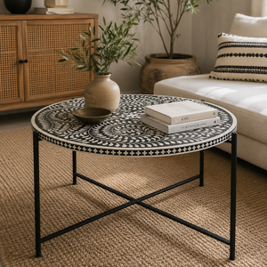 Round coffee table with a black and white geometric bone-inlay top and a black metal frame, styled in a cozy living room next to a white sofa.