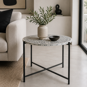 A round side table with a black metal frame and a patterned gray and white top, styled in a modern living room with a vase of greenery and a small bowl on top.
