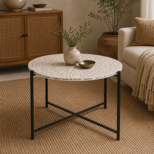 Round coffee table with a white and beige patterned stone top and a black metal frame, styled in a warm, neutral-toned living room next to a sofa.