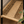 Close-up of a woven rattan or wicker shelf with a black metal frame, placed on a wood floor next to a woven basket and a plant.