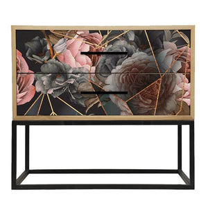 A wooden pedestal bedside table with a floral design on the drawers and a geometric pattern, placed on a black metal frame.